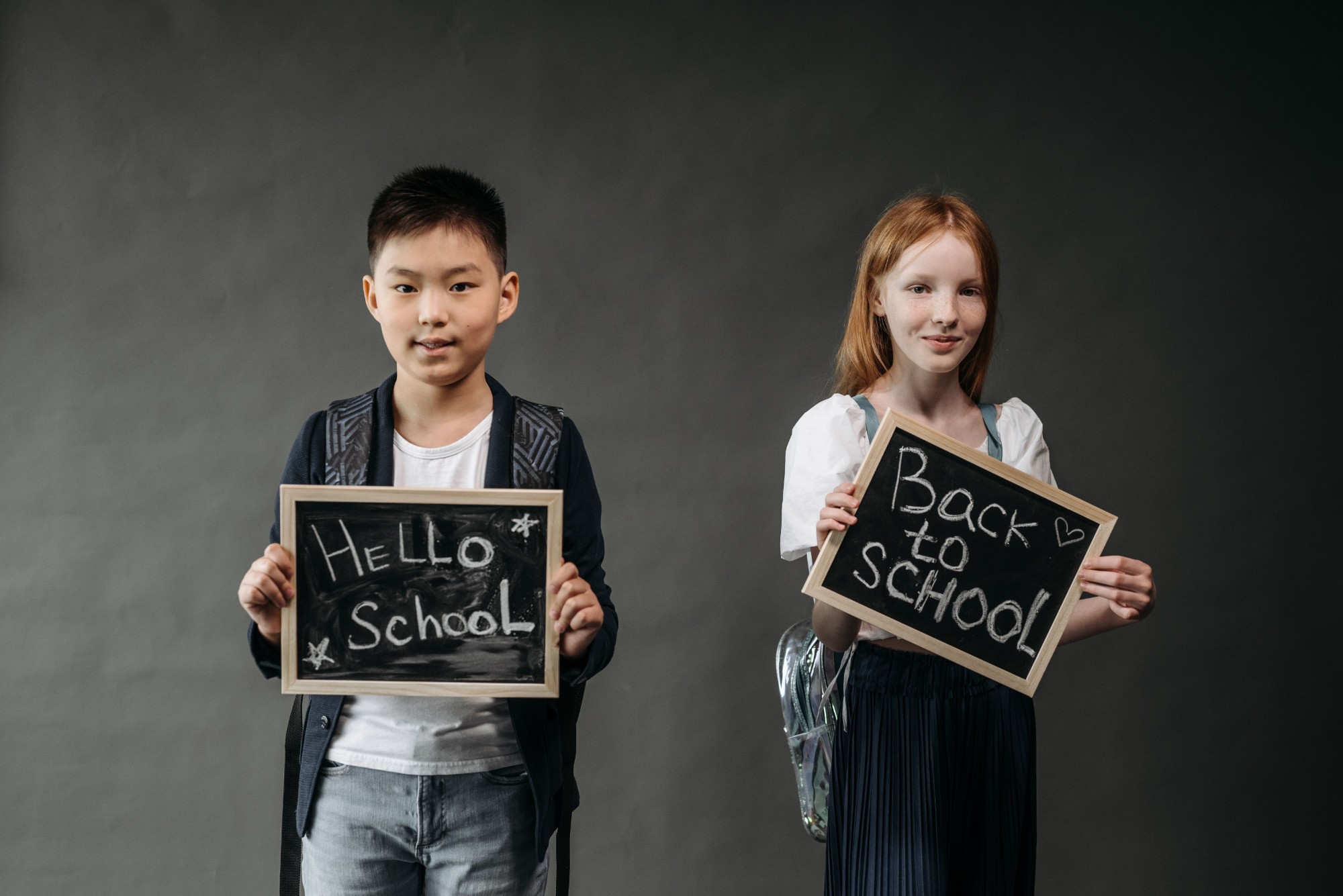 Dois alunos a segurar ardósias com as mensagens "Hello School" e "Back to School"